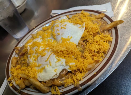 A plate of fries topped with cheese, gravy, and two poached eggs, served on a diner-style plate.