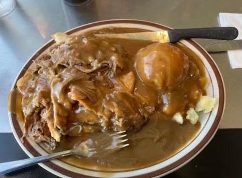 A plate of meatloaf covered in gravy, served with mashed potatoes and a side of gravy, on a diner-style plate.