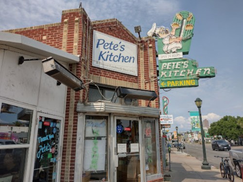 Exterior of Pete's Kitchen, a brick building with a neon sign, featuring a parking sign and a clear blue sky.