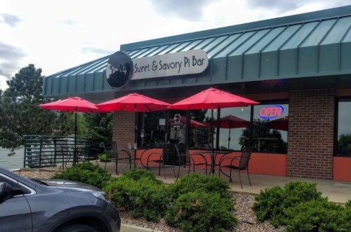 Exterior of Sweet & Savory Pi Bar with red umbrellas, outdoor seating, and an "Open" sign.