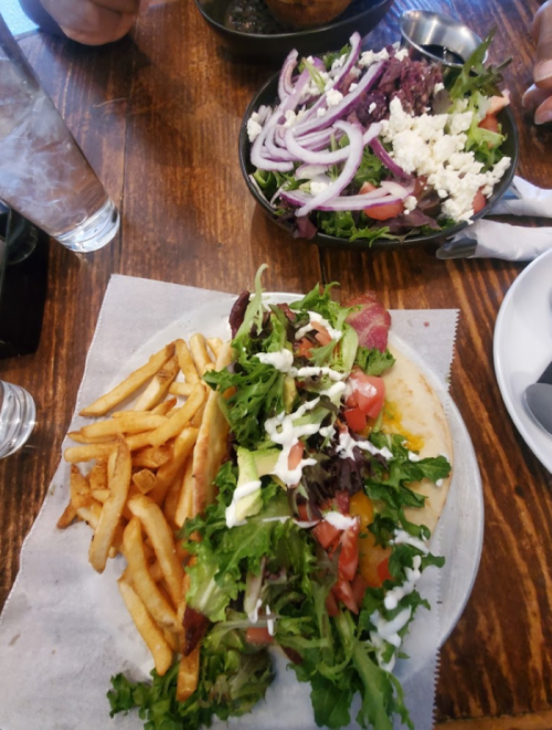 A plate with a large sandwich topped with lettuce, tomatoes, and sauce, served with fries and a side salad.