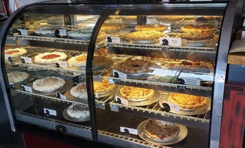 A display case filled with various pies, including fruit and cream varieties, neatly arranged on shelves.