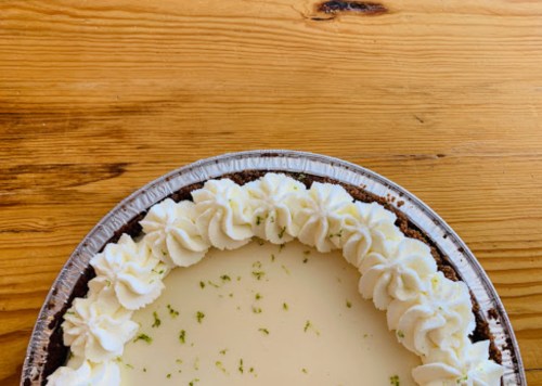 A close-up of a creamy pie topped with whipped cream, set on a wooden table.