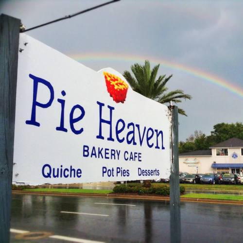 Sign for "Pie Heaven Bakery Cafe" with offerings like quiche, pot pies, and desserts, under a rainbow.