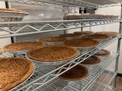 A rack filled with various baked pies in metal tins, showcasing a variety of crusts and fillings.