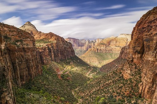 A panoramic view of Zion National Park, showcasing towering red rock cliffs and a lush green valley below.