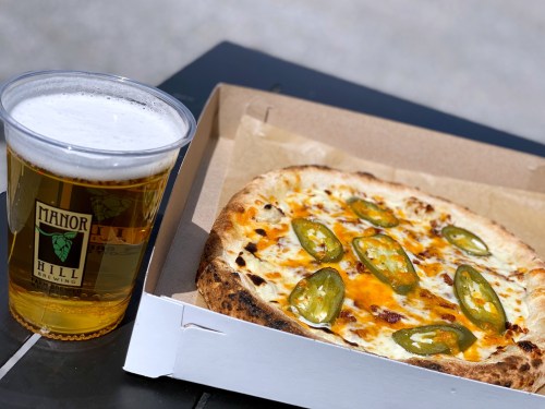 A slice of pizza topped with jalapeños next to a glass of beer on a table.