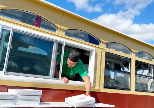 A person in a green shirt leans out of a window, placing a white box on a table outside a colorful building.
