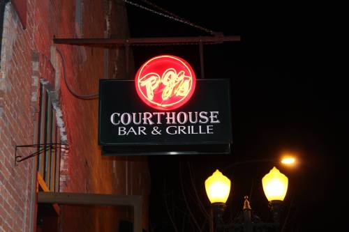 Neon sign for "PJ's Courthouse Bar & Grille" illuminated at night, hanging from a brick building.