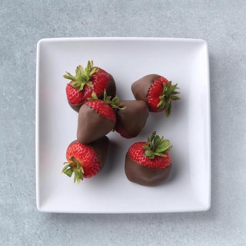 A white plate with six chocolate-covered strawberries arranged neatly.