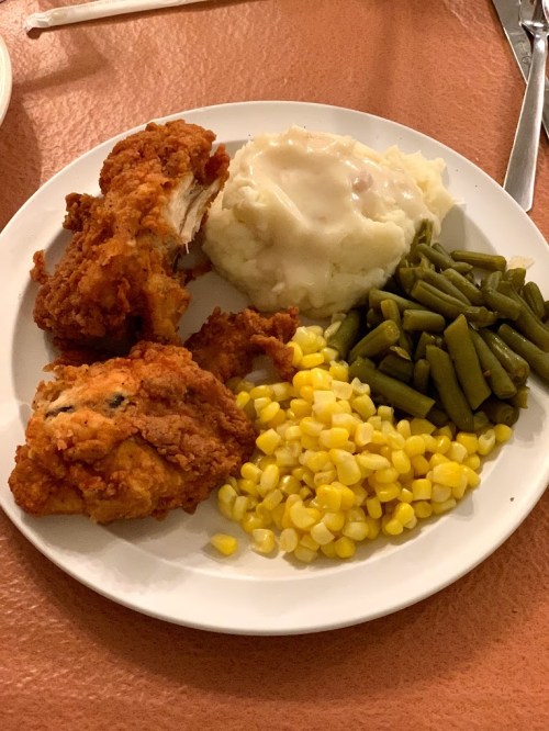 A plate of fried chicken, mashed potatoes with gravy, green beans, and corn.