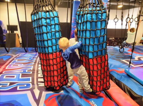 A child plays between two large, colorful netted structures in a fun indoor activity space.