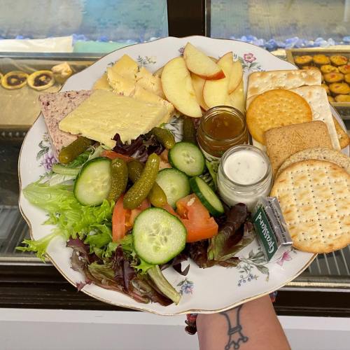 A plate of assorted cheeses, crackers, salad, pickles, apple slices, and dips, held in a hand.