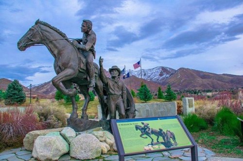 A bronze statue of a mounted rider and a standing figure, with mountains and flags in the background.