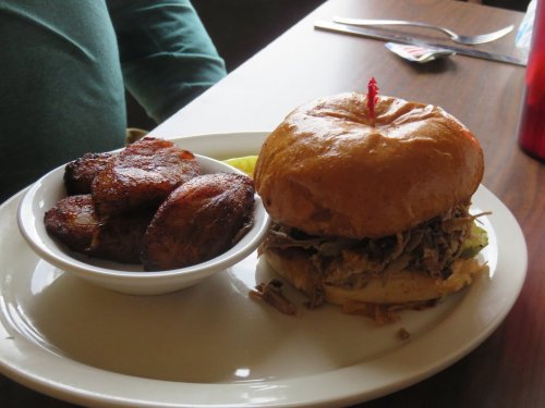 A pulled pork sandwich with a cherry on top, served with a side of crispy fried plantains.