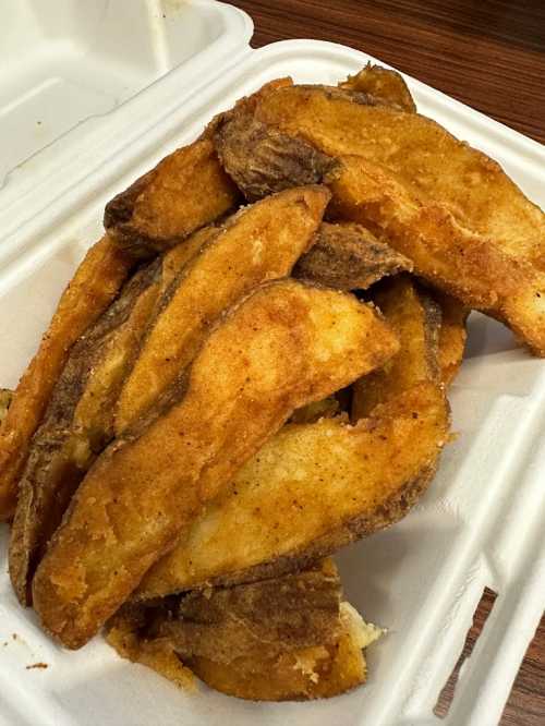 A pile of golden-brown fried fish fillets in a white takeout container.