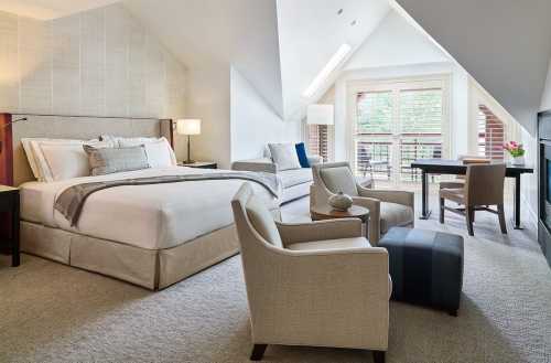 A cozy hotel room featuring a king bed, seating area, desk, and large windows with natural light.