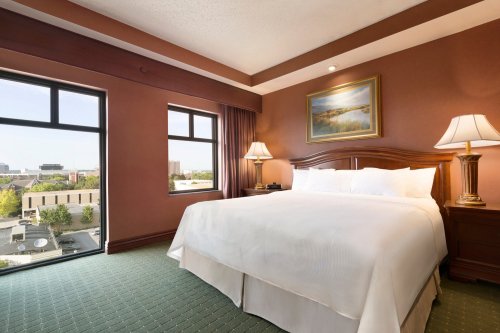 A cozy hotel room featuring a large bed, two lamps, and windows with a view of the city.