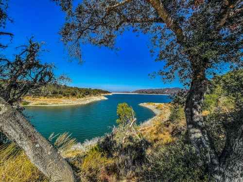 A serene lake view framed by trees, with clear blue skies and distant hills in the background.