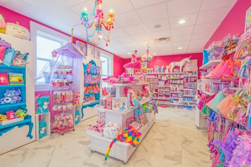 Brightly colored toy store interior with plush toys, costumes, and vibrant decor, featuring pink walls and chandeliers.