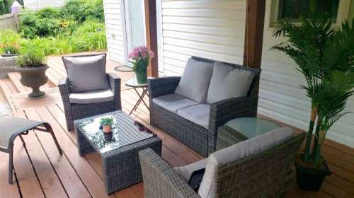Cozy outdoor seating area with wicker furniture, a glass table, and potted plants on a wooden deck.