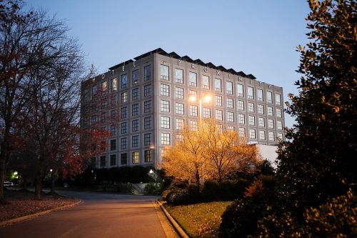 A modern hotel building at dusk, surrounded by trees and soft lighting, with a clear sky in the background.