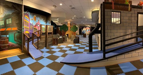 A colorful indoor play area with murals, ramps, and soft flooring, designed for children's activities and exploration.