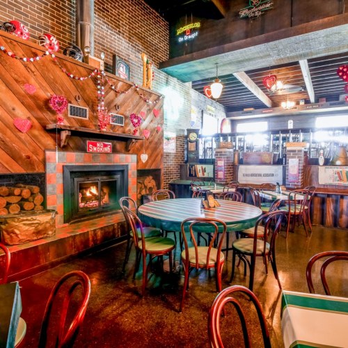 Cozy restaurant interior with a fireplace, decorated with hearts, and tables set for dining. Warm and inviting atmosphere.