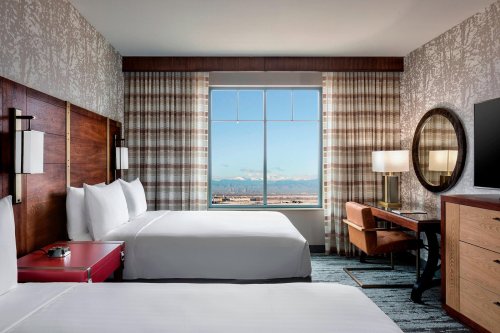 A modern hotel room with two beds, a desk, and a large window showcasing a mountain view.
