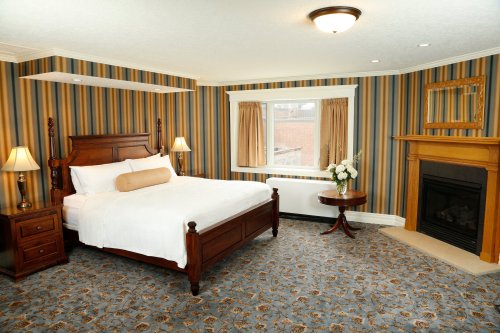 Cozy hotel room with a king bed, striped wallpaper, fireplace, and a small table with flowers.