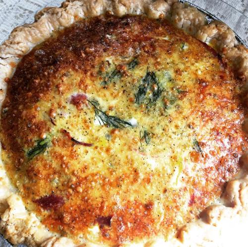 A golden-brown quiche with a flaky crust, topped with herbs and a cheesy, savory filling.