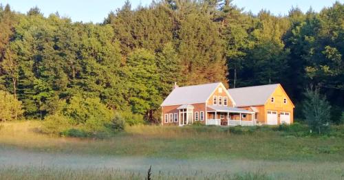 A charming house with a porch sits in a lush green field, surrounded by trees under a clear blue sky.