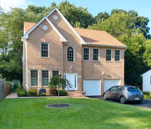 A two-story brick house with a sloped roof, large windows, and a well-maintained lawn and driveway.