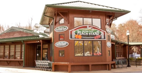 A wooden building with signs for a peach stand, restaurant, and butcher shop, surrounded by trees.