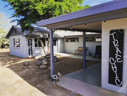 A cozy outdoor view of a welcoming home with a porch, decorative signs, and a small dog near the entrance.