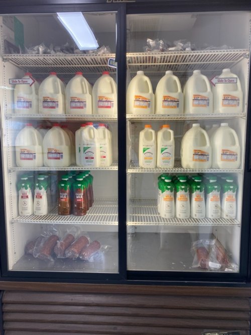 Refrigerator display with various milk jugs, juice bottles, and packaged sausages on shelves.