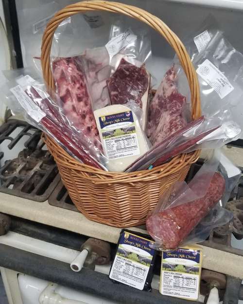 A woven basket filled with various packaged meats and cheese, resting on a stove.