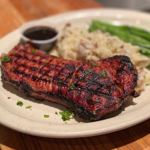 Grilled steak on a plate with mashed potatoes, green beans, and a small cup of sauce. Garnished with parsley.