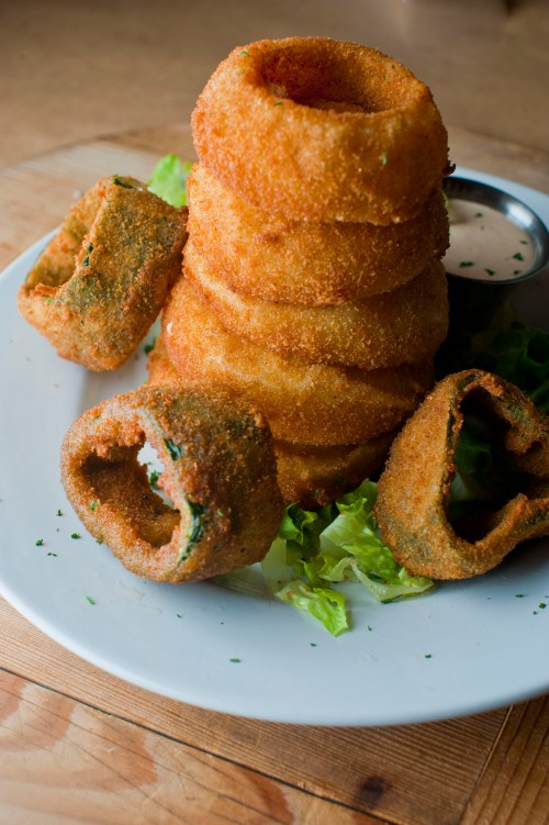 A plate of crispy onion rings stacked on lettuce, accompanied by a small bowl of dipping sauce.
