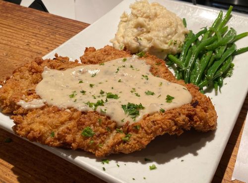 A plate of fried chicken topped with creamy gravy, served with mashed potatoes and green beans.