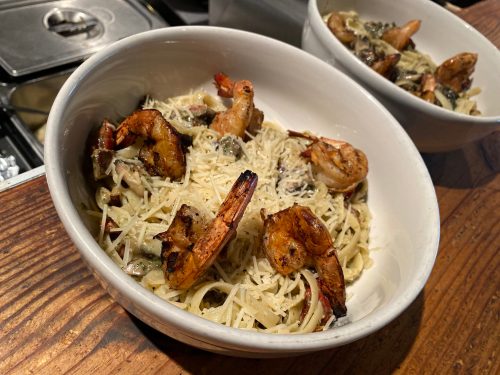 A bowl of pasta with shrimp, topped with grated cheese and herbs, served on a wooden table.