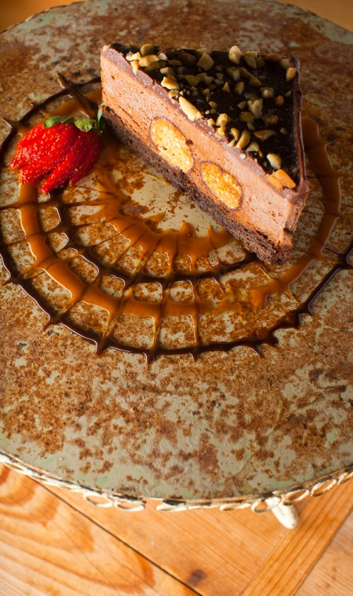 A slice of chocolate cake topped with nuts and a strawberry, served on a decorative plate with caramel drizzle.
