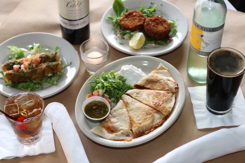 A table setting with wine, a green salad, crab cakes, a plate of quesadillas, and drinks, including a cocktail and beer.