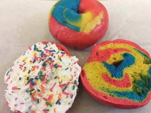 A colorful bagel with vibrant swirls of red, blue, and yellow, alongside a frosted bagel topped with sprinkles.