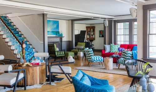 Bright and stylish living room with colorful furniture, a piano, and a staircase featuring blue and white patterned steps.
