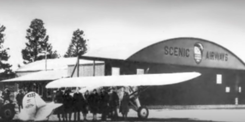 Black and white photo of a vintage airplane and a group of people in front of a hangar labeled "Scenic Airways."