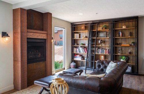 Cozy living room with a leather sofa, fireplace, and a bookshelf filled with books and decorative items.