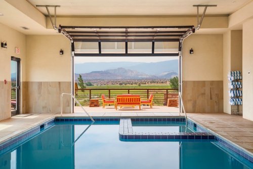 Indoor pool with a view of mountains and a patio area featuring orange seating. Bright and inviting atmosphere.
