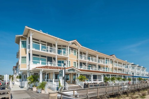 A coastal building with multiple balconies and large windows, surrounded by palm trees and a wooden walkway.