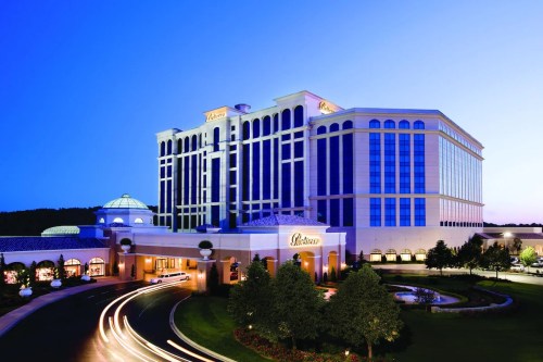 A modern hotel and casino building illuminated at dusk, surrounded by landscaped gardens and a winding driveway.
